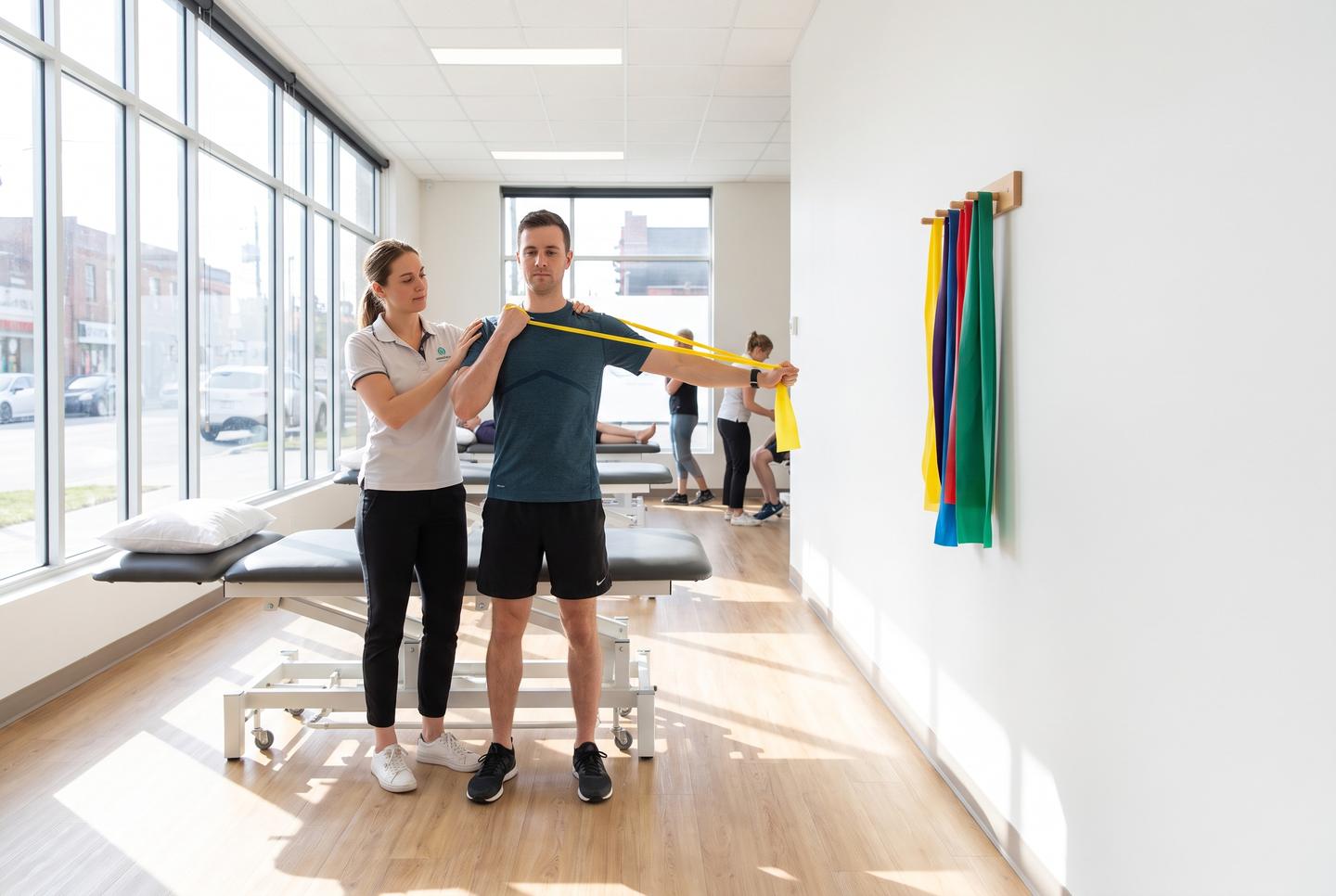 Symbolbild Physiotherapie: Physiotherapeutin leitet einen Patienten bei einer Übung mit dem Gymnastikband an